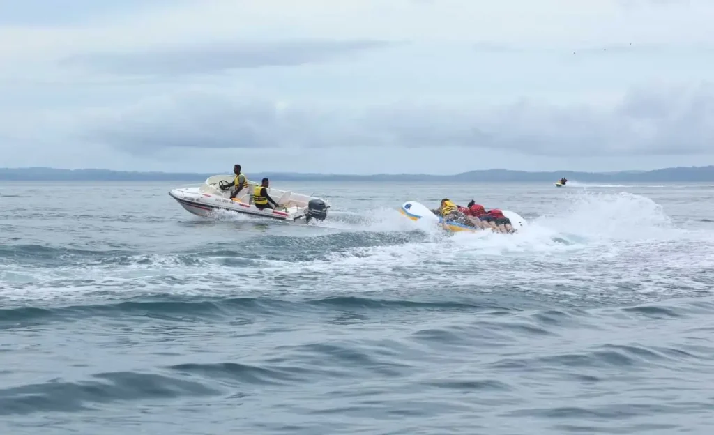 people lying on a rubber cushion being pulled by a speed boat
