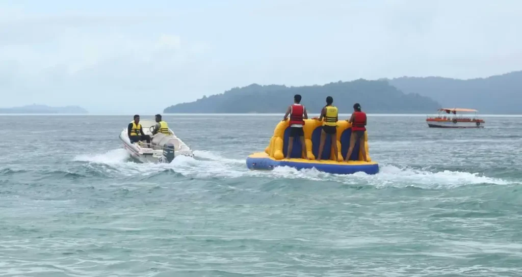 3 people standing on a rubber cusion being dragged by a speed boat